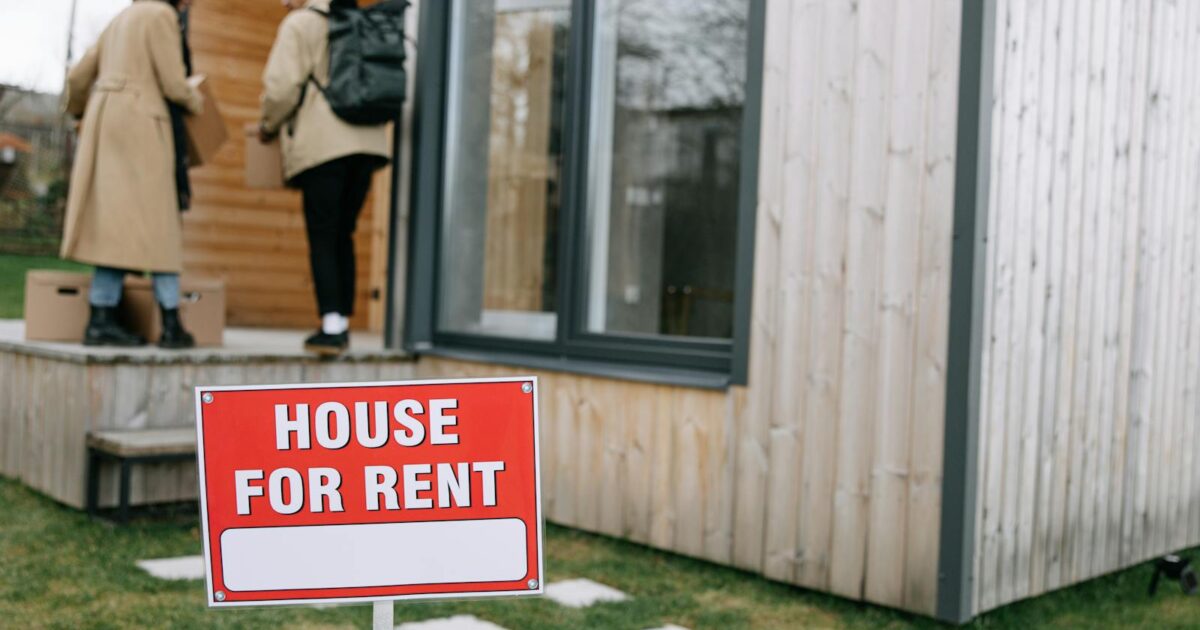 A couple entering a modern wooden house for rent, carrying boxes.